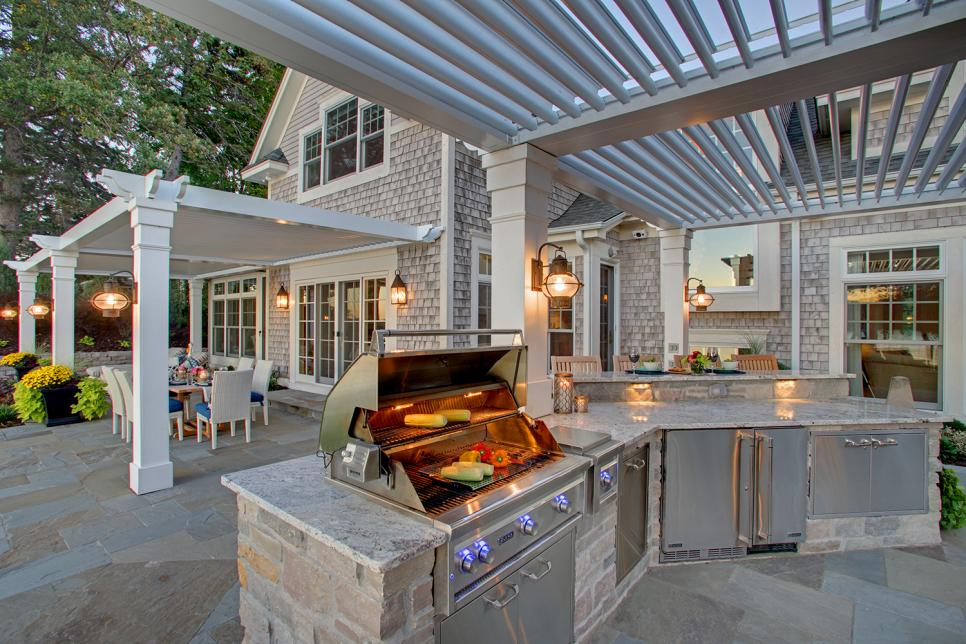 Large luxury outdoor kitchen with built-in stainless steel grill, stone island, and pergola patio at a Lake Travis home in Austin, Texas — by Infinit Interiors